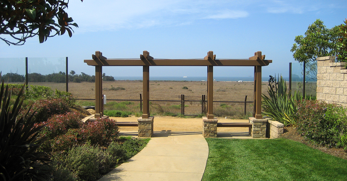Pergola over drive way with open field and ocean in the background